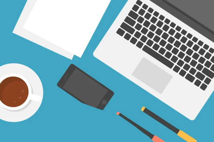 Open laptop and writing utensils, cup of coffee on a desk