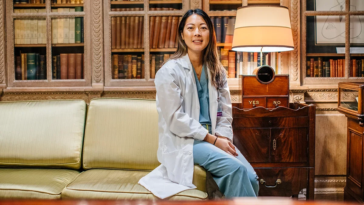 Woman resident sitting in a research room, in scrubs and a white coat