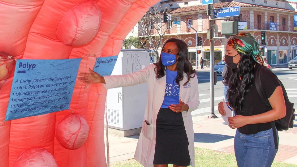How to Prevent Cancer Via Lifestyle Choices. People look at a colon cancer awareness display