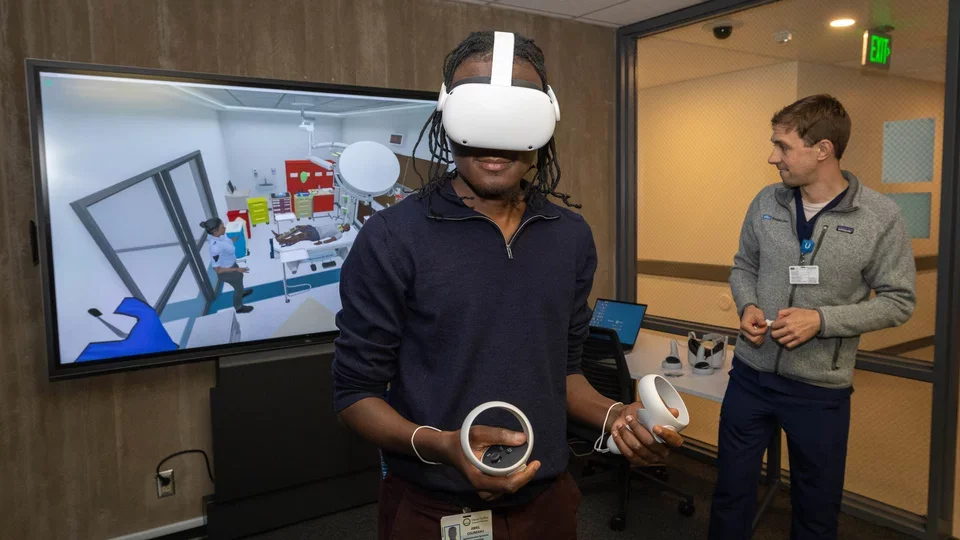 Anesthesiology administrative specialist Jibril Osumanu, left, wears a VR headset for an immersive 3D medical simulation scenario alongside Daniel Weisman, simulation center learning experience designer and station facilitator.