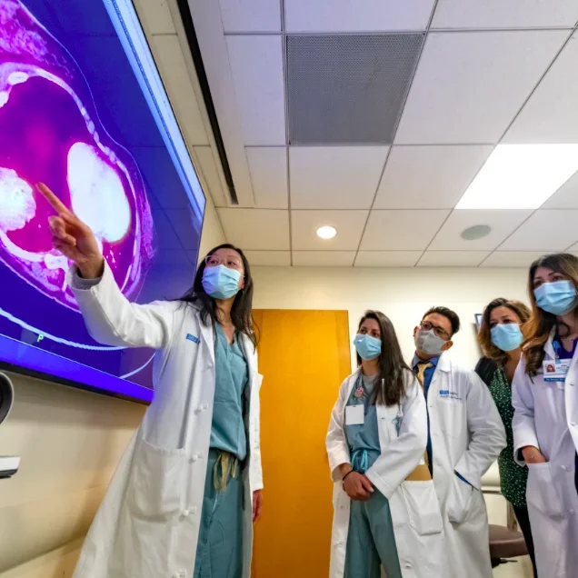 A group of masked residents and physicians reviewing results on a large digital screen