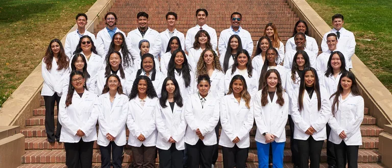 The 2025 cohort of SHPEP Scholars standing in their white coats on Janns Steps at UCLA.