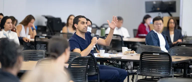 A man in a blue shirt communicates with a group, sharing insights with an engaged audience.