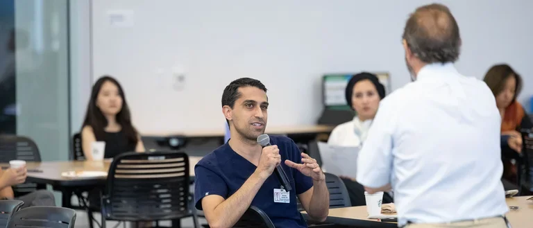 Dr. Madrenas in conversation with a group of attentive individuals and speaking to an person in scrubs 