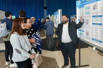 Man in suit explaining research poster to two women
