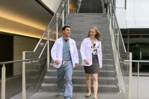 Two medical students walk down the stairs into the courtyard at Geffen Hall, deep in conversation