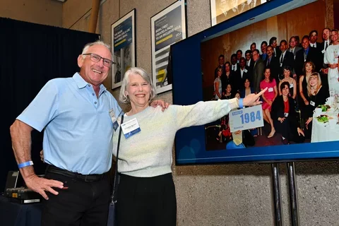 two alumni pointing to a photo of themselves on a screen