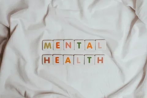 the words mental health written in tiles with different colored letters laid out on a sheet of cloth. "mental" is on top of "health"