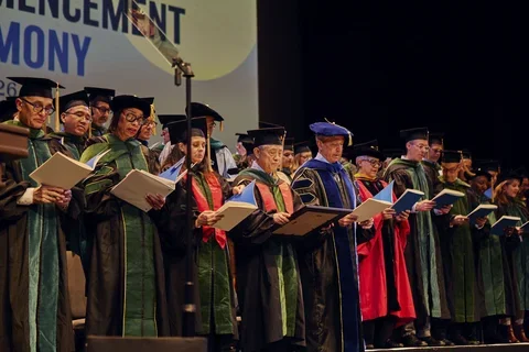 : Award-winners Jessica B. O'Connell, MD (front row, third from the left) and Kat-Kit Hui, MD (front row, fourth from the left) join graduating doctors in reciting the Oath of Hippocrates at the 2026 commencement ceremony.