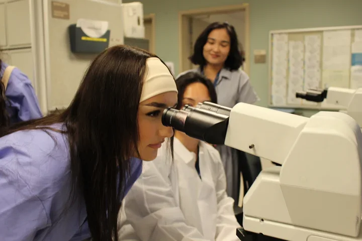 A student wearing scrubs looks into a microscope
