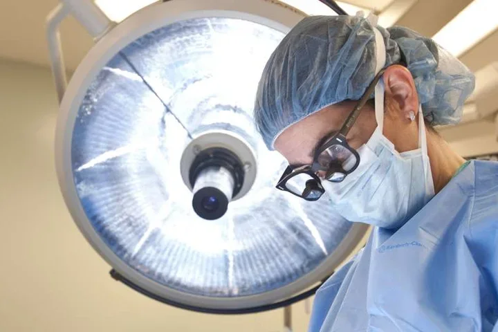 Photo of Doctor in surgery with surgical lamp behind them 