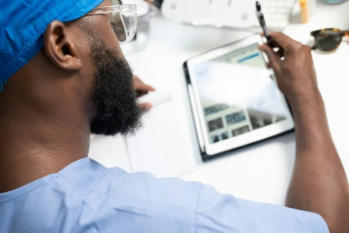A physician wearing scrubs reviews information on a tablet