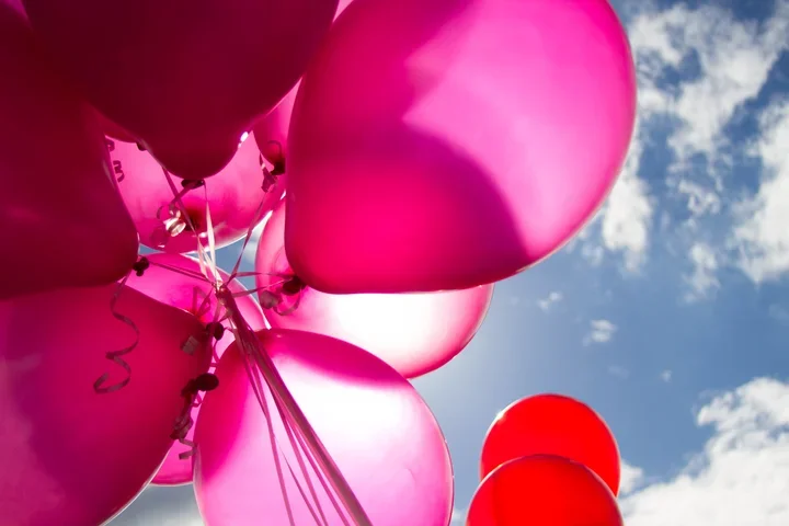 Hot pink balloons floating in a sunny blue sky