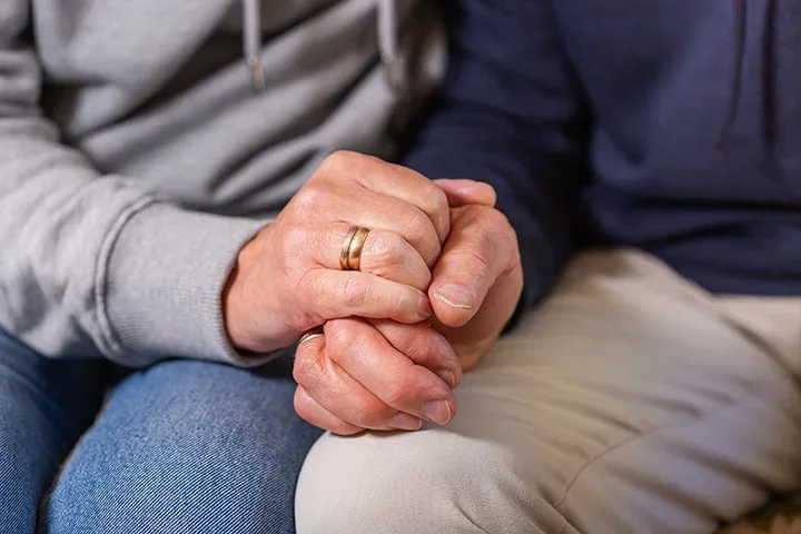 Spouse holding hands resting on legs