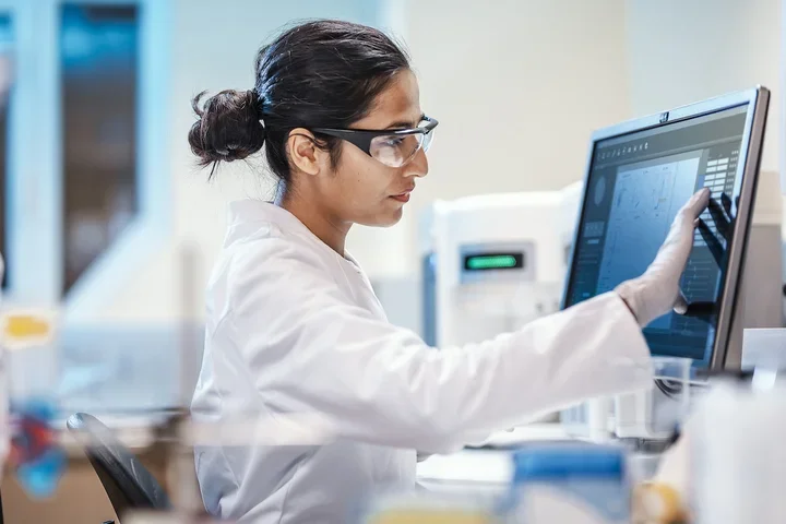 Female scientist in safety glasses working on a digital screen