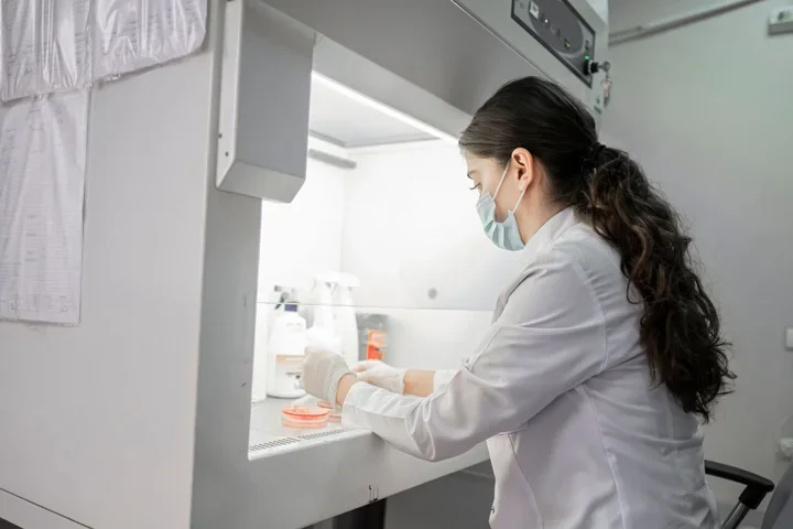 Woman with long dark hair doing research under lab fume hood