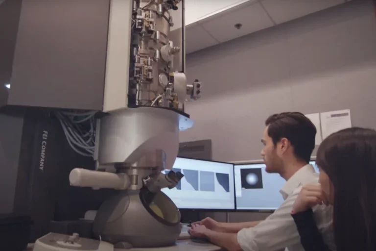 Two researchers review data on the screen of a large, powerful microscope"