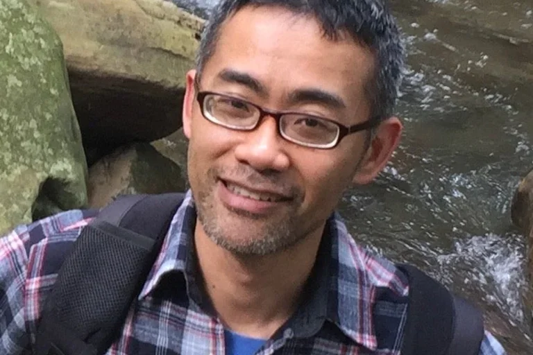Man with glasses and collar-plaid shirt with river in the background