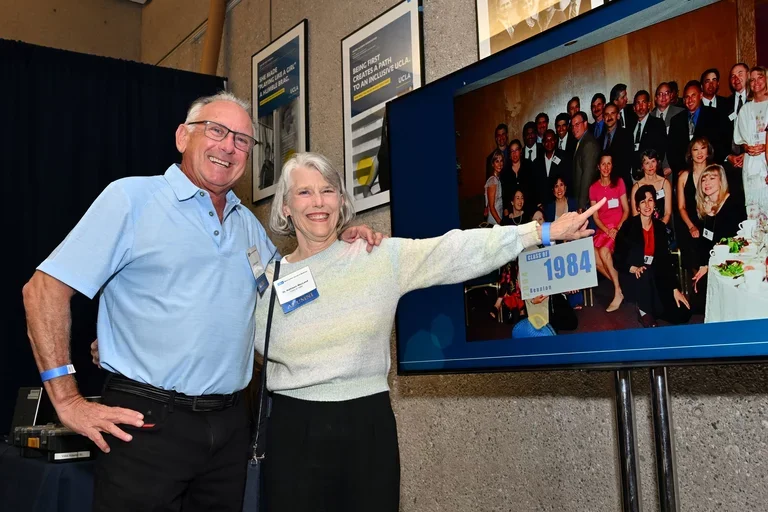 two alumni pointing to a photo of themselves on a screen