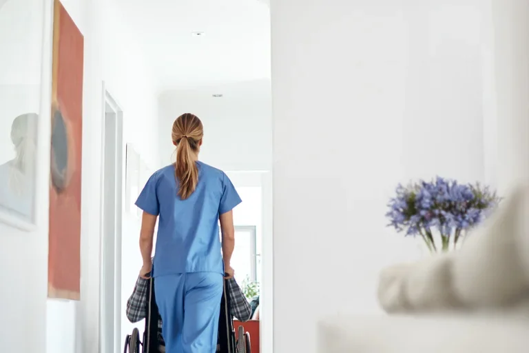 A patient in a wheelchair pushed by a nurse wearing scrubs