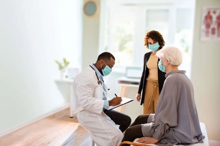 Masked physician writing in a chart while patients and caregivers look on