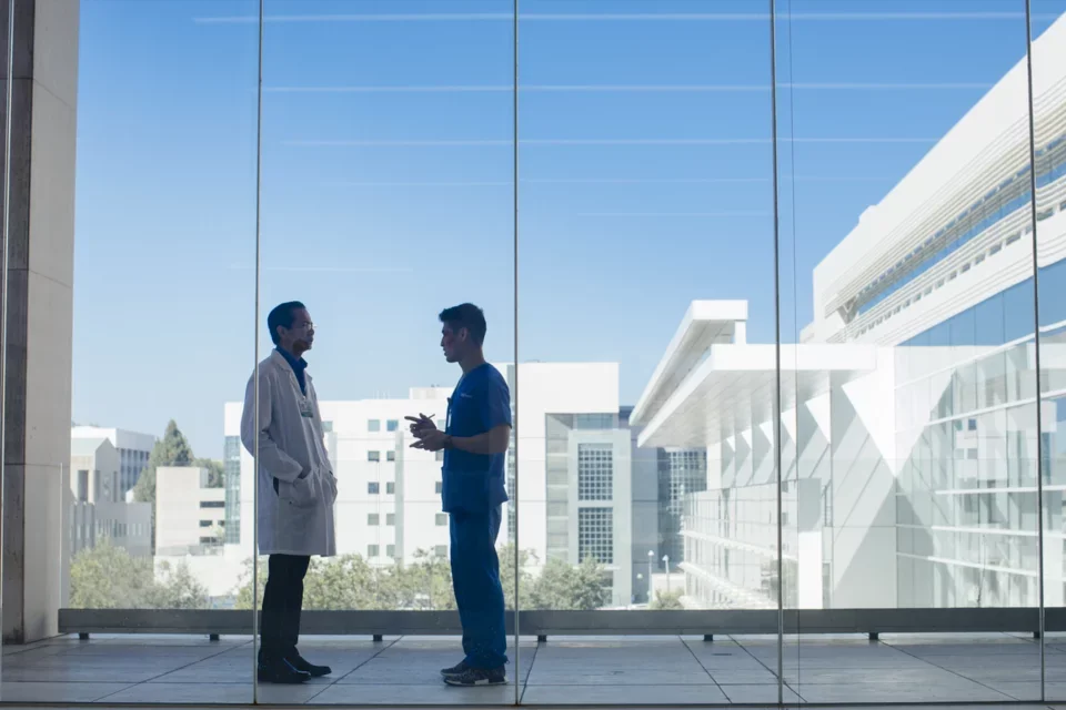 A resident and an attending physician take a moment to confer in a hallway overlooking campus