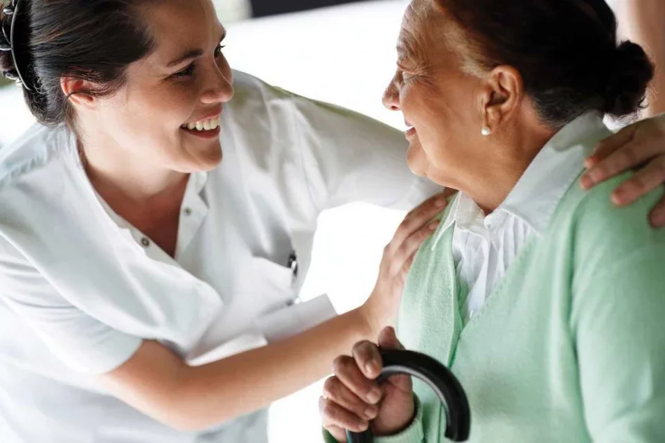 Treatment for Alzheimer's Disease Caregiver in White Scrubs Embraces Elderly Female Patient