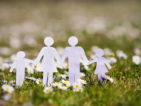 paper bodies of family holding hands over grass and flowers in spring
