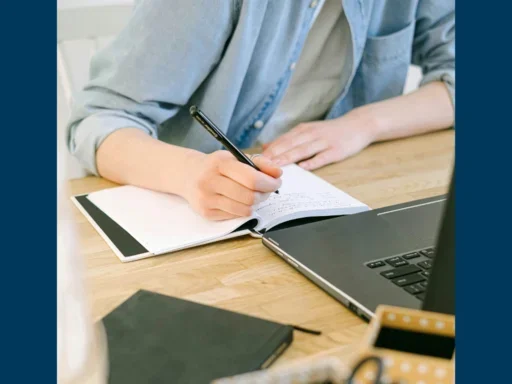 Man writing on a piece of paper in front of a laptop with stationary around him.