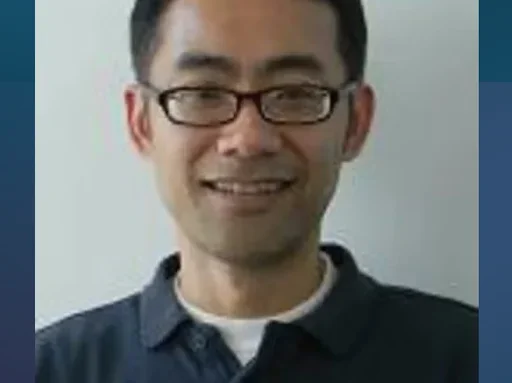 Man's face smiling with glasses and dark hair with blue collared shirt