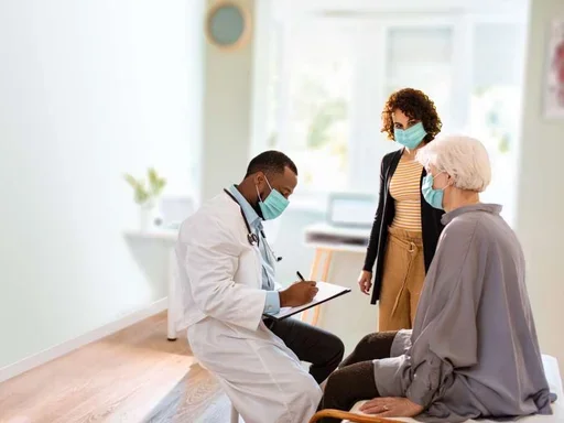 Masked physician writing in a chart while patients and caregivers look on