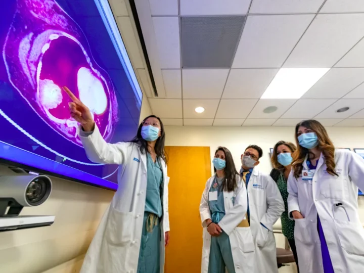 A group of masked residents and physicians reviewing results on a large digital screen