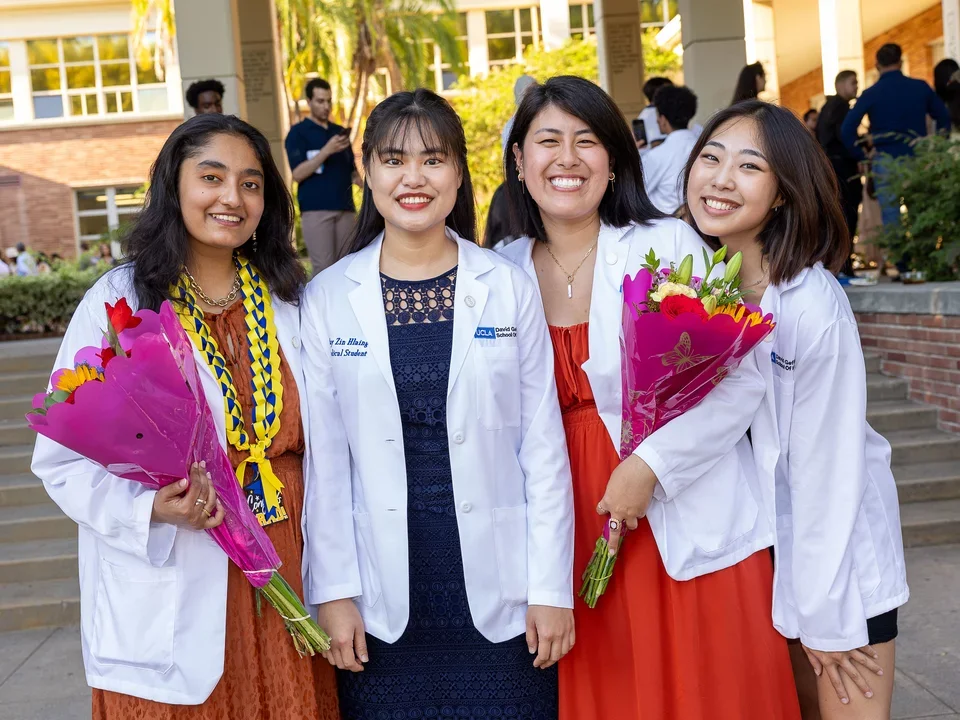 Four Students Smiling in White Coats at Annual Ceremony