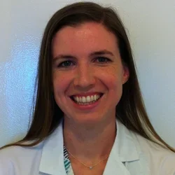 Dr. Sarah Gustafson smiling portrait in front of white wall wearing white coat