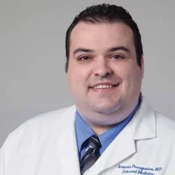 Dr. Sarah Gustafson smiling portrait in front of grey portrait wearing white coat
