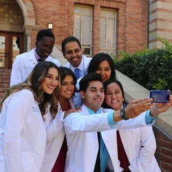 A group of medical students wearing white coats pose for a selfie after the white coat ceremony.