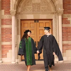UCLA residents and med-school alumni Makana Williams and Rigoberto Perez Hernandez smile at each other wearing graduation robes in front of an academic building. 