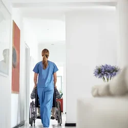 A patient in a wheelchair pushed by a nurse wearing scrubs