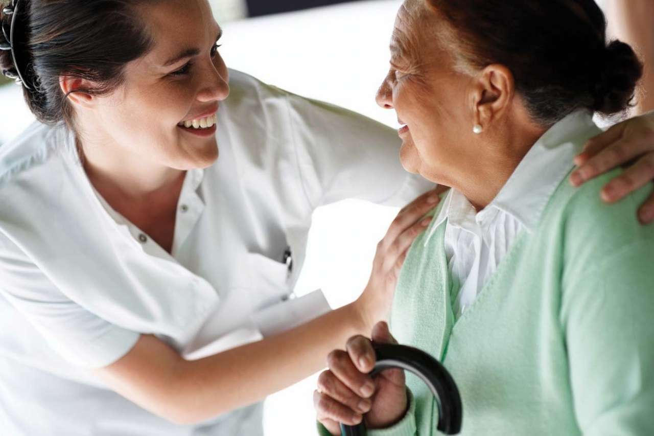 Treatment for Alzheimer's Disease Caregiver in White Scrubs Embraces Elderly Female Patient