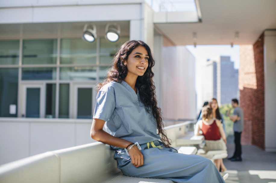 A visiting medical student (VSLO) in scrubs in the courtyard of Geffen Hall