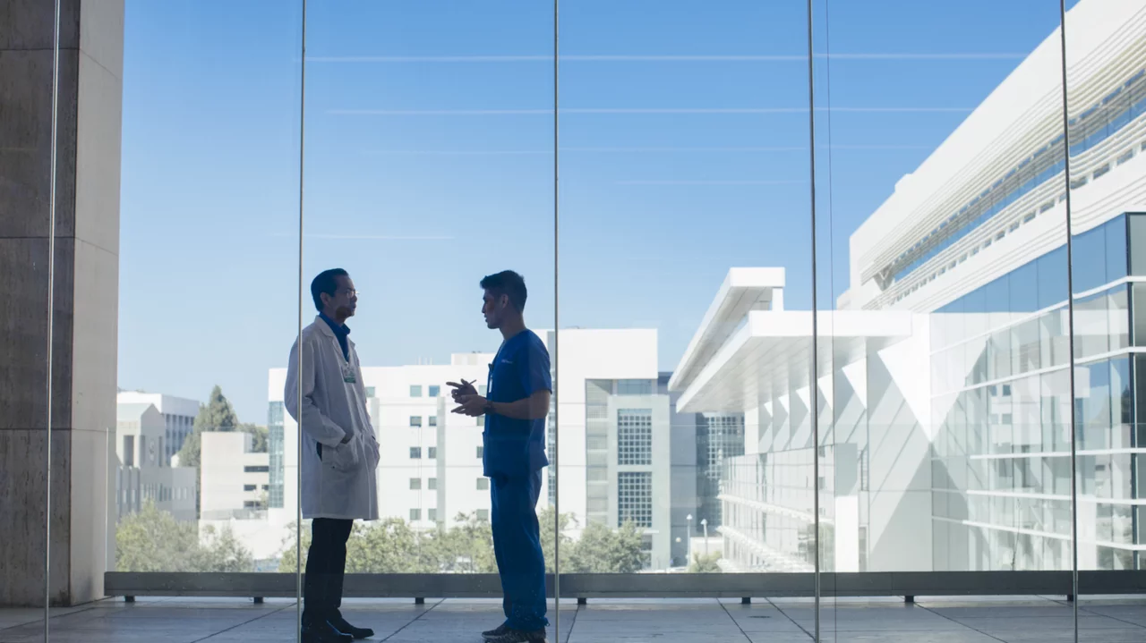 A resident and an attending physician take a moment to confer in a hallway overlooking campus