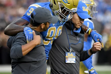 Sports medicine professionals helping an injured UCLA football player off the field 