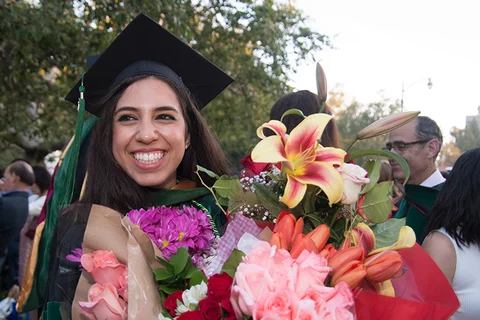 A graduating student holds a large bouquet of flowers after the commencement ceremony.