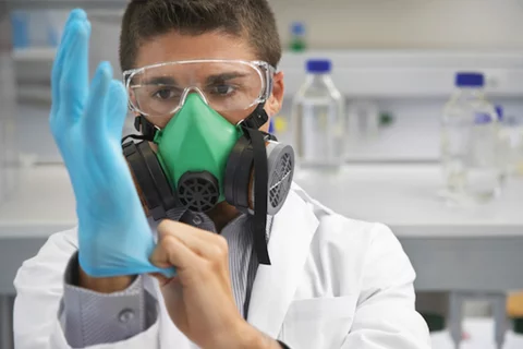 Lab member in a white lab coat, wearing full PPE and putting on latex gloves