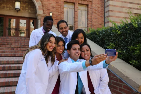 A group of medical students wearing white coats pose for a selfie after the white coat ceremony.