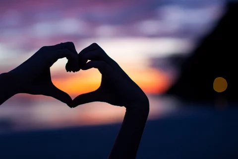 Two hands creating a heart in front of a sunset