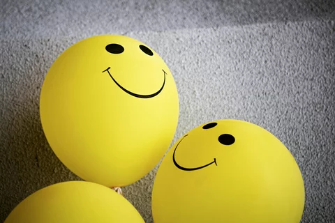 2 yellow balloons with black smiley faces on them slightly turned to face each other