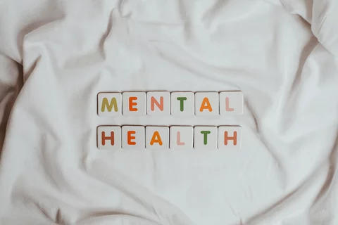 the words mental health written in tiles with different colored letters laid out on a sheet of cloth. "mental" is on top of "health"