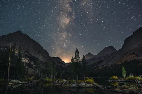 starry night sky with mountains and a lake at the bottom of the image
