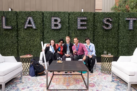 5 People sitting on a couch together and smiling with letters that spell out "LA BEST" above them.